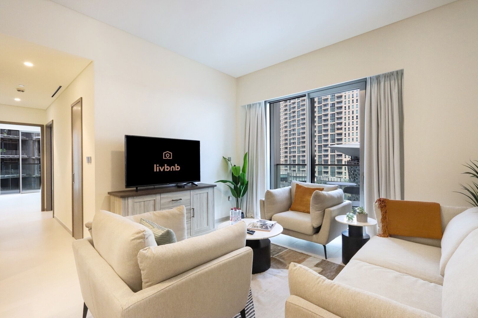 Een moderne woonkamer met een flatscreen televisie, twee banken, een salontafel en uitzicht op een stadsgezicht door grote ramen.