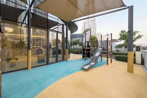Ein Spielbereich im Freien mit Rutsche, Klettergerüst und einem Glasgebäude im Hintergrund.