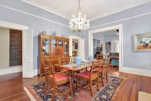 A dining room with a wooden table, chairs, a chandelier, and a patterned rug.