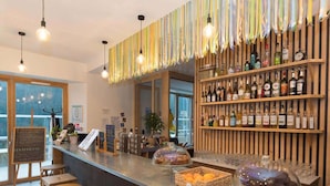 A bar area with a wooden counter, shelves of liquor bottles, and hanging light fixtures. - La Grange à Gaby (Engins)