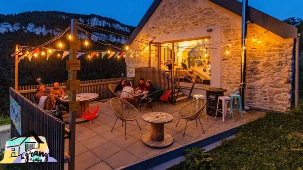 An outdoor seating area with tables and chairs, a stone building with a sloped roof, and string lights. - La Grange à Gaby (Engins)