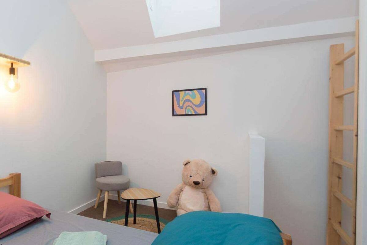 A small, cozy room with a bed, a chair, a teddy bear, and a small table.