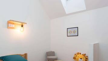A bedroom with a skylight, a bedside lamp, a framed picture, a plush toy, and a small round table.