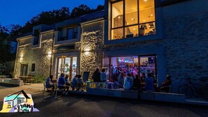 A building with large windows and a stone facade, featuring an outdoor seating area with tables and chairs. - La Grange à Gaby (Engins)