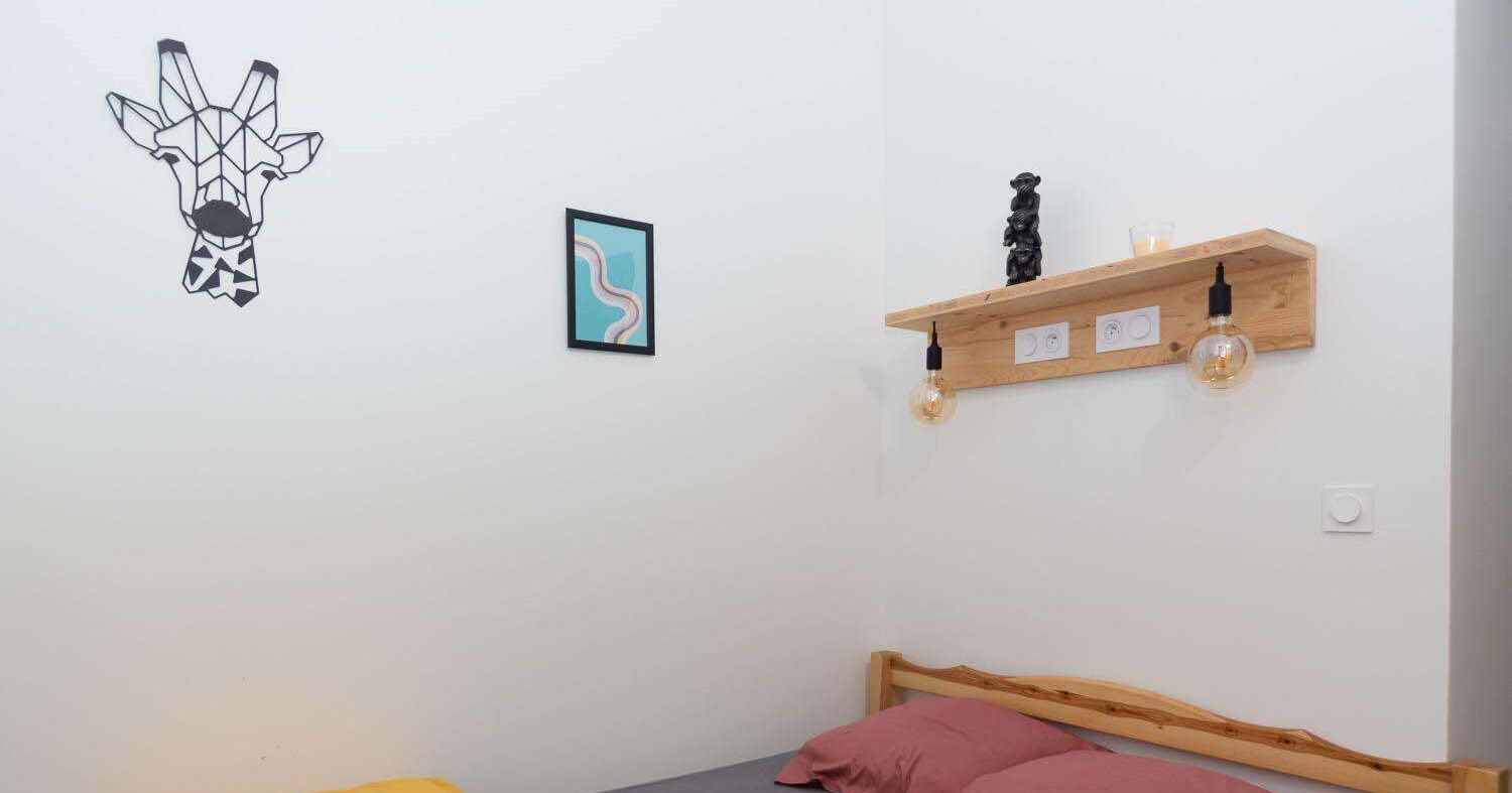 Un dormitorio con una cama de madera, un estante en la pared con objetos decorativos y una obra de arte en la pared.
