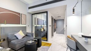 A modern hotel room with a grey sofa, a dining table, and a small coffee table. There is a large mirror on the wall and a door leading to another room. - Studio with City Views & Modern Amenities in MAG 318, Business Bay (Business Bay)