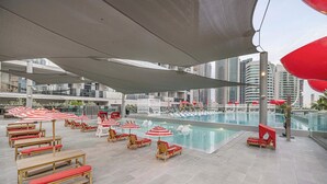 A rooftop pool area with lounge chairs and umbrellas, surrounded by modern buildings. - Studio with City Views & Modern Amenities in MAG 318, Business Bay (Business Bay)