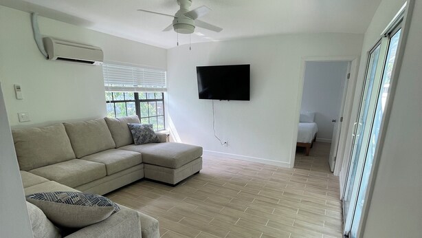A spacious living area with a sectional sofa, a small table, a ceiling fan, and a flat-screen TV mounted on the wall. - 1 block to the beach, perfect! (Cocoa Beach)