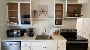 A compact kitchen with white cabinets, a built-in microwave, a coffee maker, a sink, and a stove. - 1 block to the beach, perfect! (Cocoa Beach)