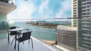 Un balcone con ringhiera in vetro che si affaccia su uno specchio d'acqua e una città in lontananza.