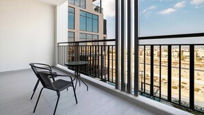 A balcony with a table and chairs, a view of a desert landscape, and a modern building in the background.