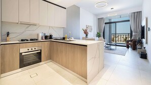 A modern kitchen with a built-in oven, a dining area with a glass table, and a balcony with curtains.