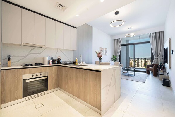 A modern kitchen with a built-in oven, a dining area with a glass table, and a balcony with curtains.