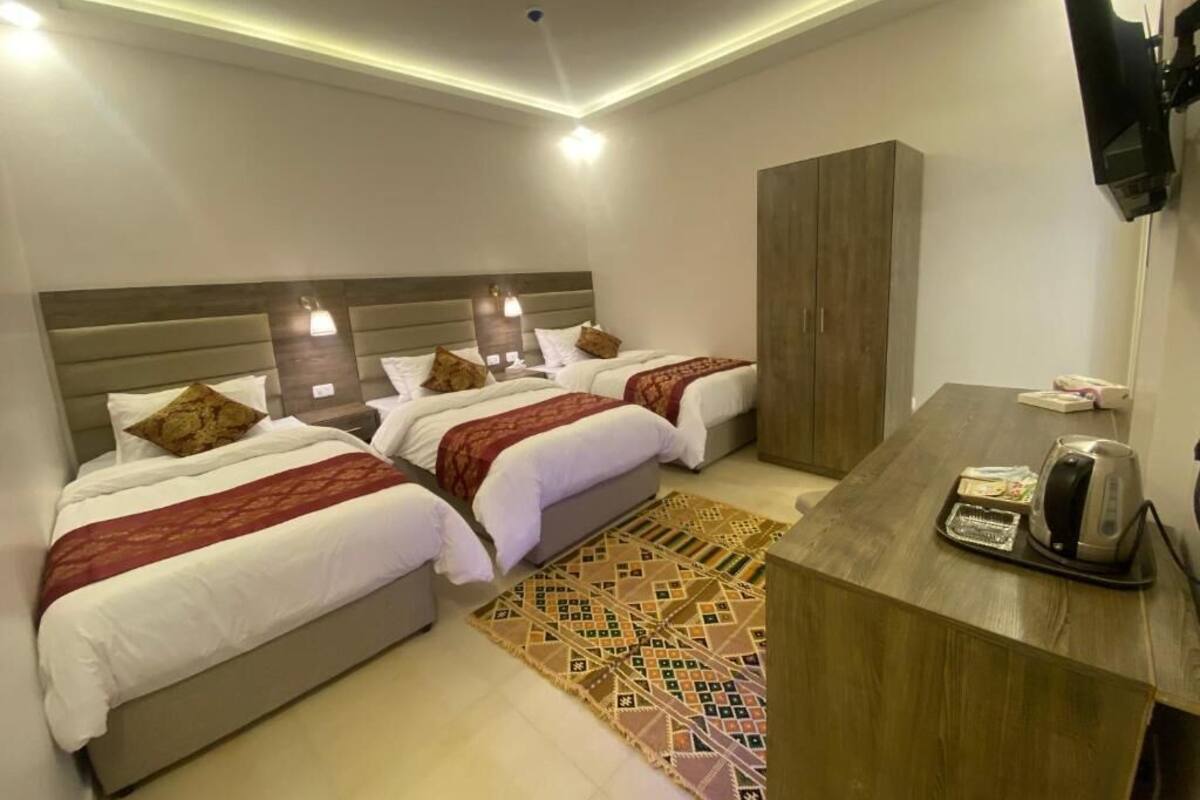 A hotel room with two beds, a wooden desk, a television, and a patterned rug.