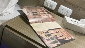 A neatly made bed with white sheets, a wooden headboard, a bedside table with a tissue box, and a power outlet. - Petra Oleander Hotel (Wadi Musa)