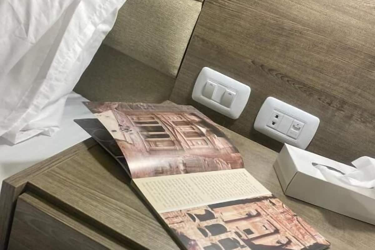 A neatly made bed with white sheets, a wooden headboard, a bedside table with a tissue box, and a power outlet.