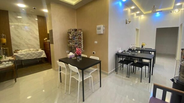 A modern dining area with a marble-tiled floor, a black dining table with white chairs, and a small side table with a vase of flowers. - Petra Oleander Hotel (Wadi Musa)