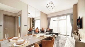 Un espace de repas moderne avec une longue table dressée pour quatre personnes, un canapé et un téléviseur fixé au mur.