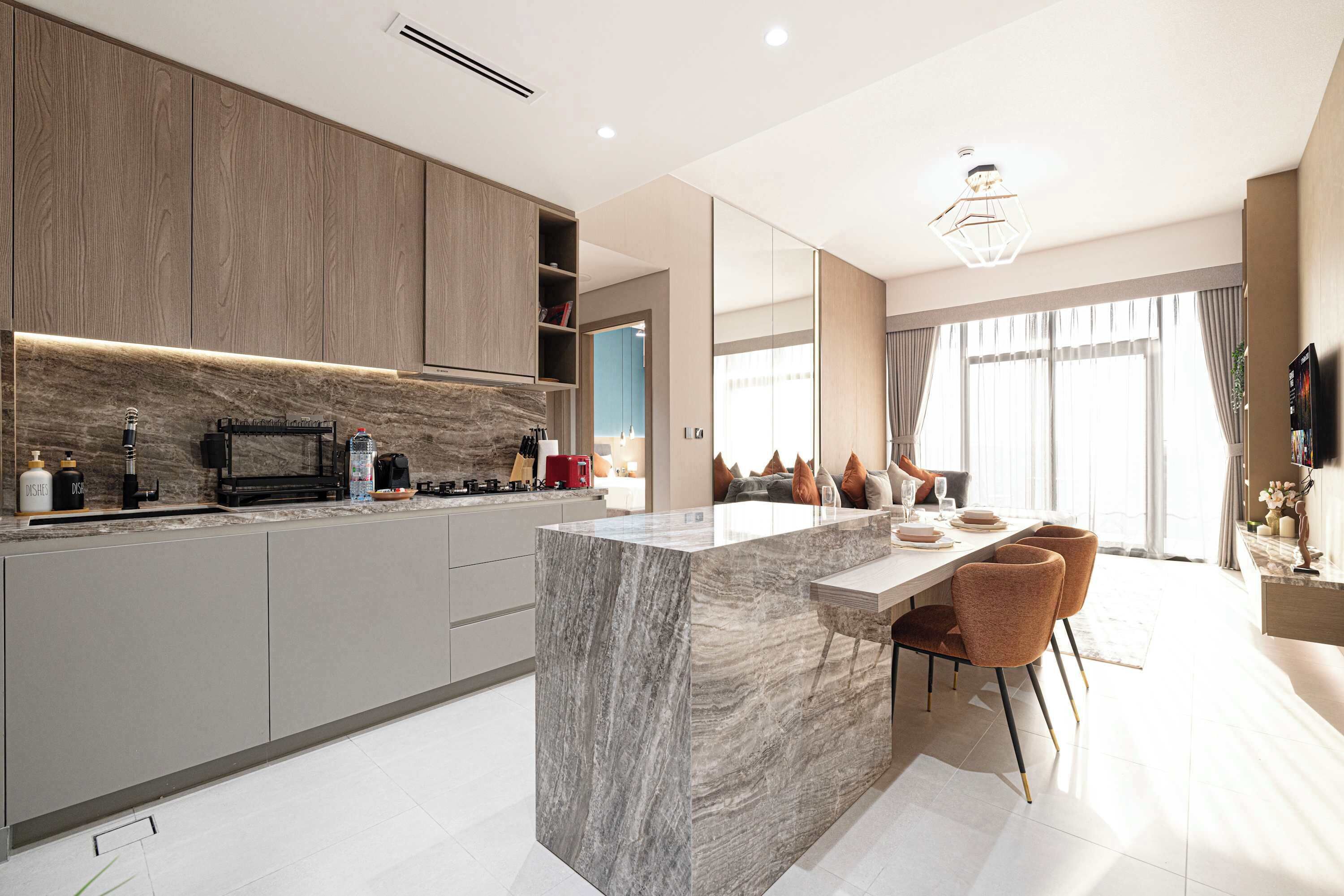 A modern kitchen with a marble island, built-in appliances, and a dining area with a large window.