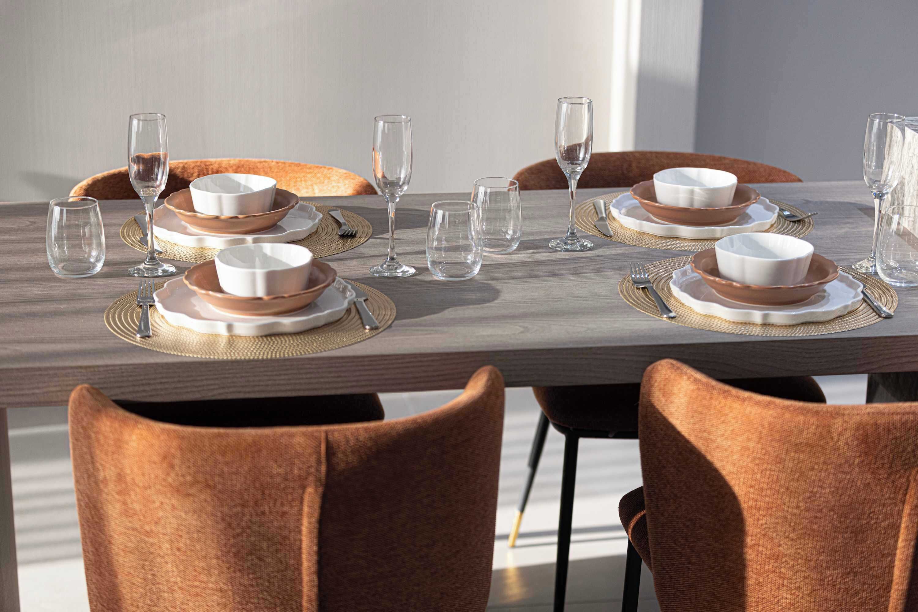 Une table à manger dressée avec des assiettes blanches et brunes, des verres transparents et un set de table en fibres tressées.
