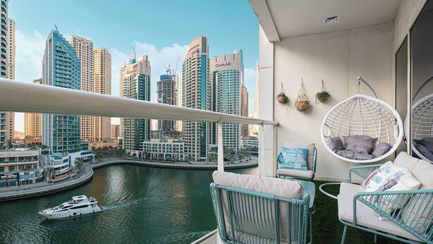 A balcony with a view of a marina and city skyline, featuring hanging chairs and a small table.