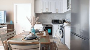 A modern kitchen with white cabinets, a stainless steel refrigerator, and a dining area with a wooden table and chairs.