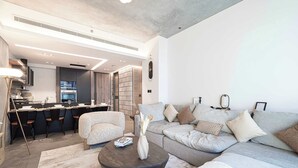 Ein modernes Wohnzimmer mit Sofa, Couchtisch und Essbereich mit Stühlen. Im Hintergrund ist eine Küche zu sehen.
