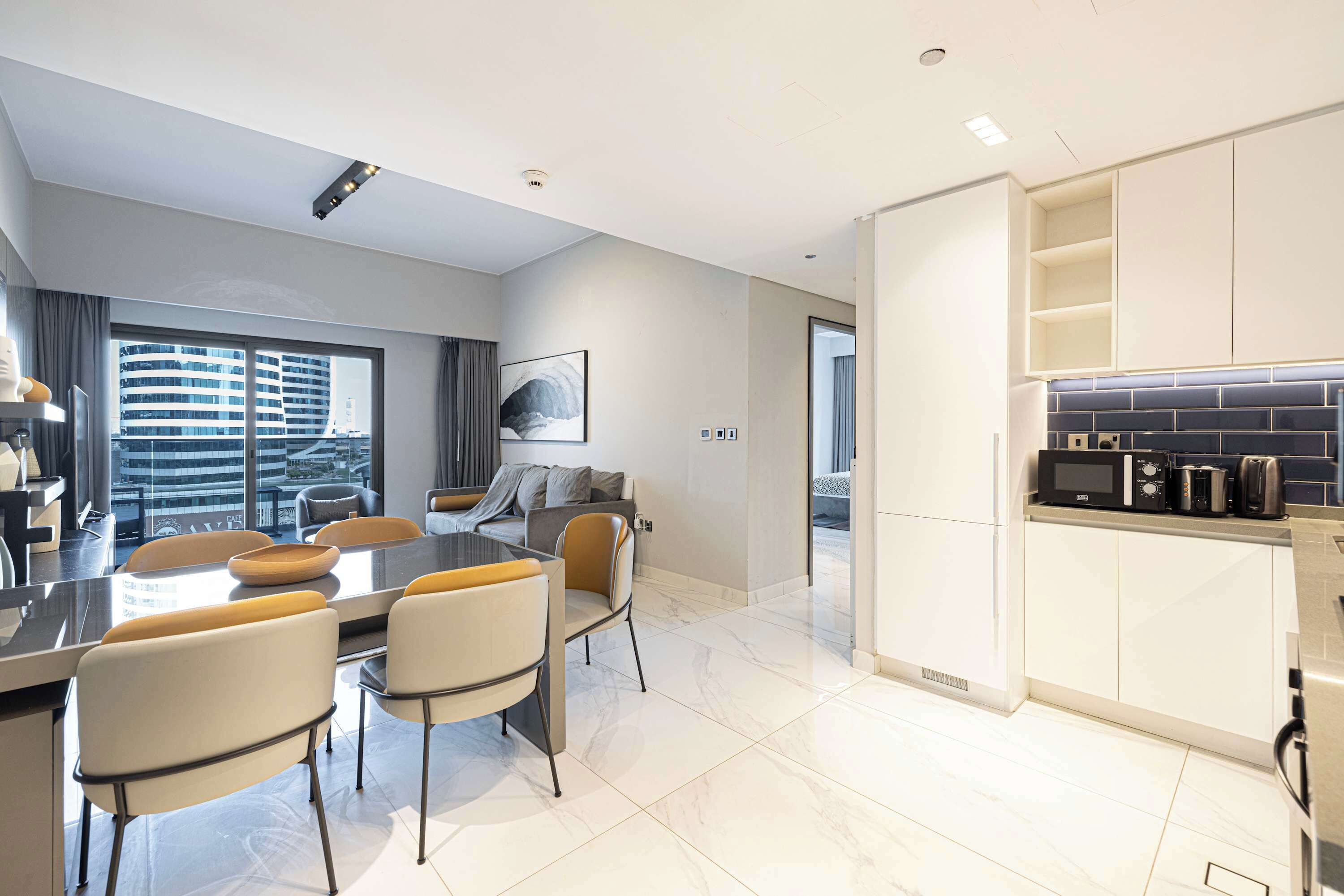 Une cuisine moderne avec des meubles blancs, un coin repas doté d’une grande table et de chaises, et une vue sur le paysage urbain par la fenêtre.