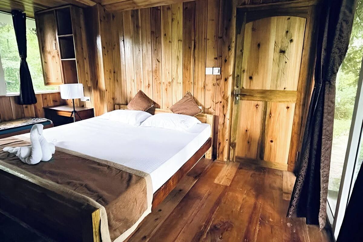 A wooden cabin bedroom with a bed, pillows, a nightstand, and a lamp.