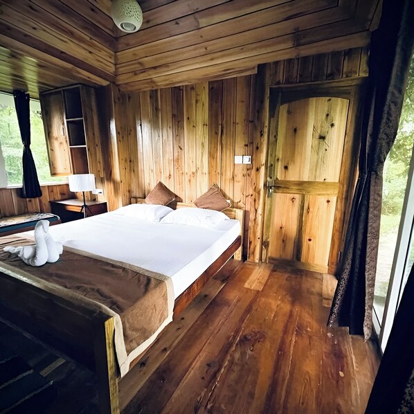 A wooden cabin bedroom with a bed, pillows, a nightstand, and a lamp. - Khachoe Residency, Ravangla (Namchi)
