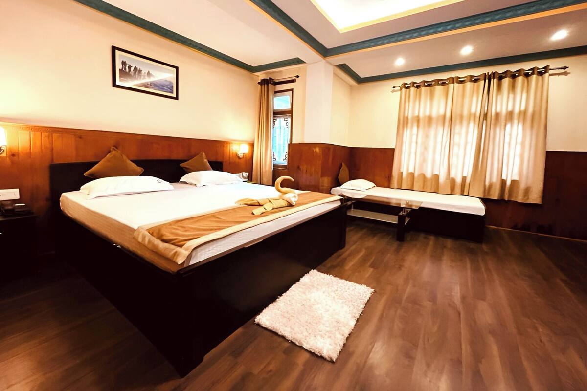 A hotel room with a large bed, a smaller bed, a desk, and a window with curtains.