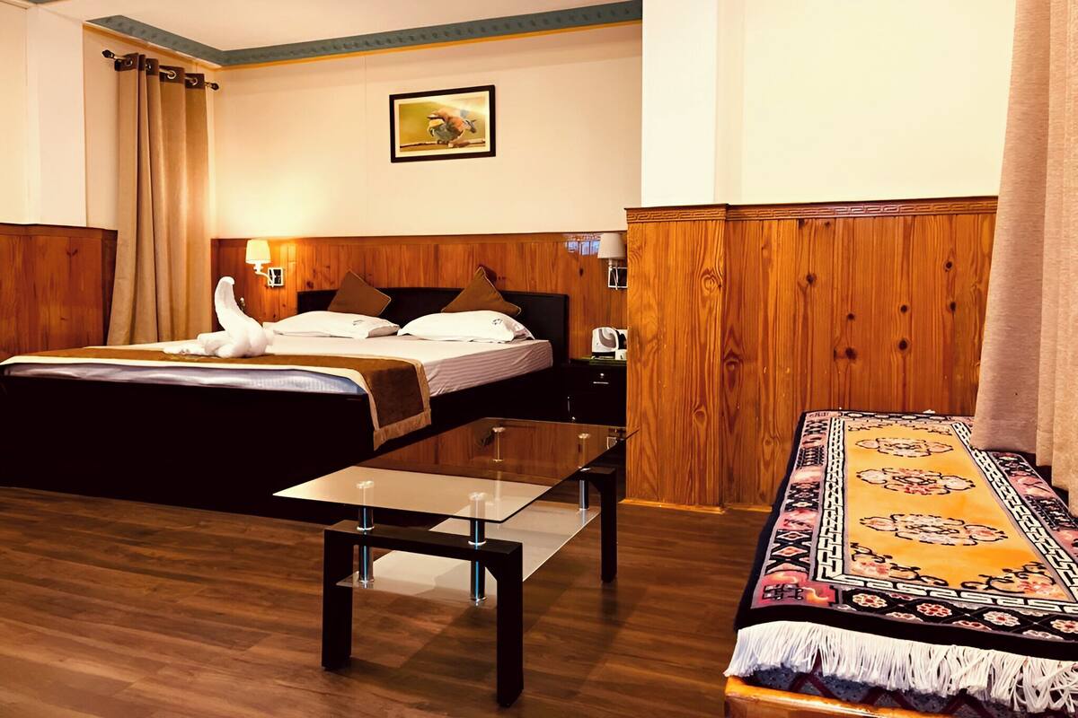 A hotel room with a wooden bed, a glass table, a patterned rug, and a wooden wardrobe.