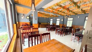 A spacious dining area with wooden tables and chairs, large windows, and a ceiling with wooden beams and hanging decorations. - Khachoe Residency, Ravangla (Namchi)