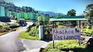 A sign for Khachoe Residency with a road leading to it, surrounded by greenery and buildings. - Khachoe Residency, Ravangla (Namchi)