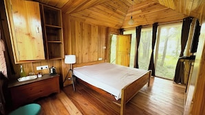 A wooden cabin bedroom with a bed, dresser, lamp, and a view of the outdoors. - Khachoe Residency, Ravangla (Namchi)
