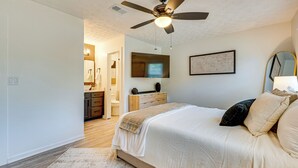 Una camera da letto con un letto, una ventola a soffitto, una televisione, un comò e uno specchio.