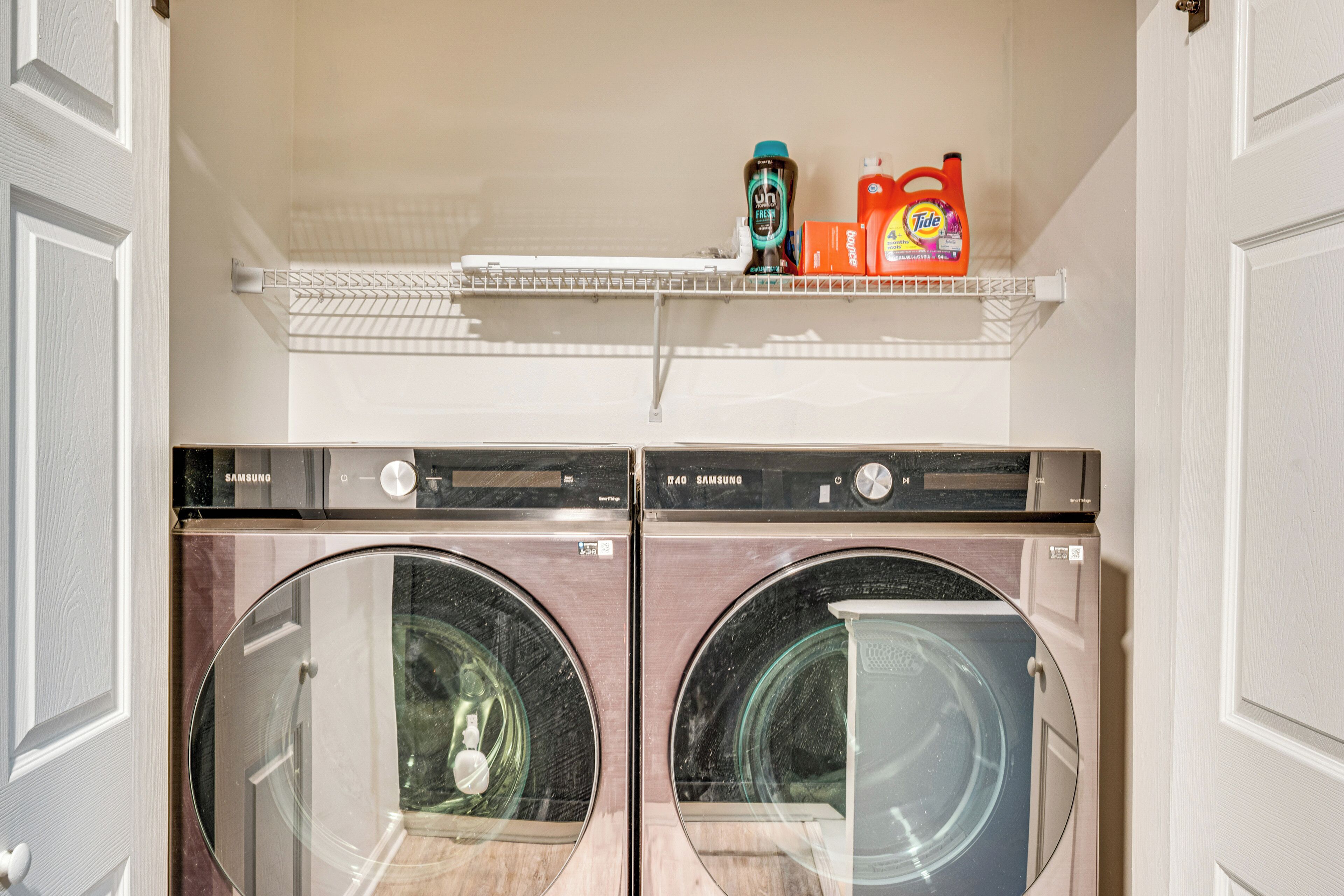 A laundry room with two front-loading washing machines, a shelf with laundry detergent, and a Samsung dryer.