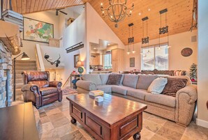 A spacious living area with a large sectional sofa, a leather armchair, and a wooden coffee table. A staircase with a wooden railing leads to an upper level.