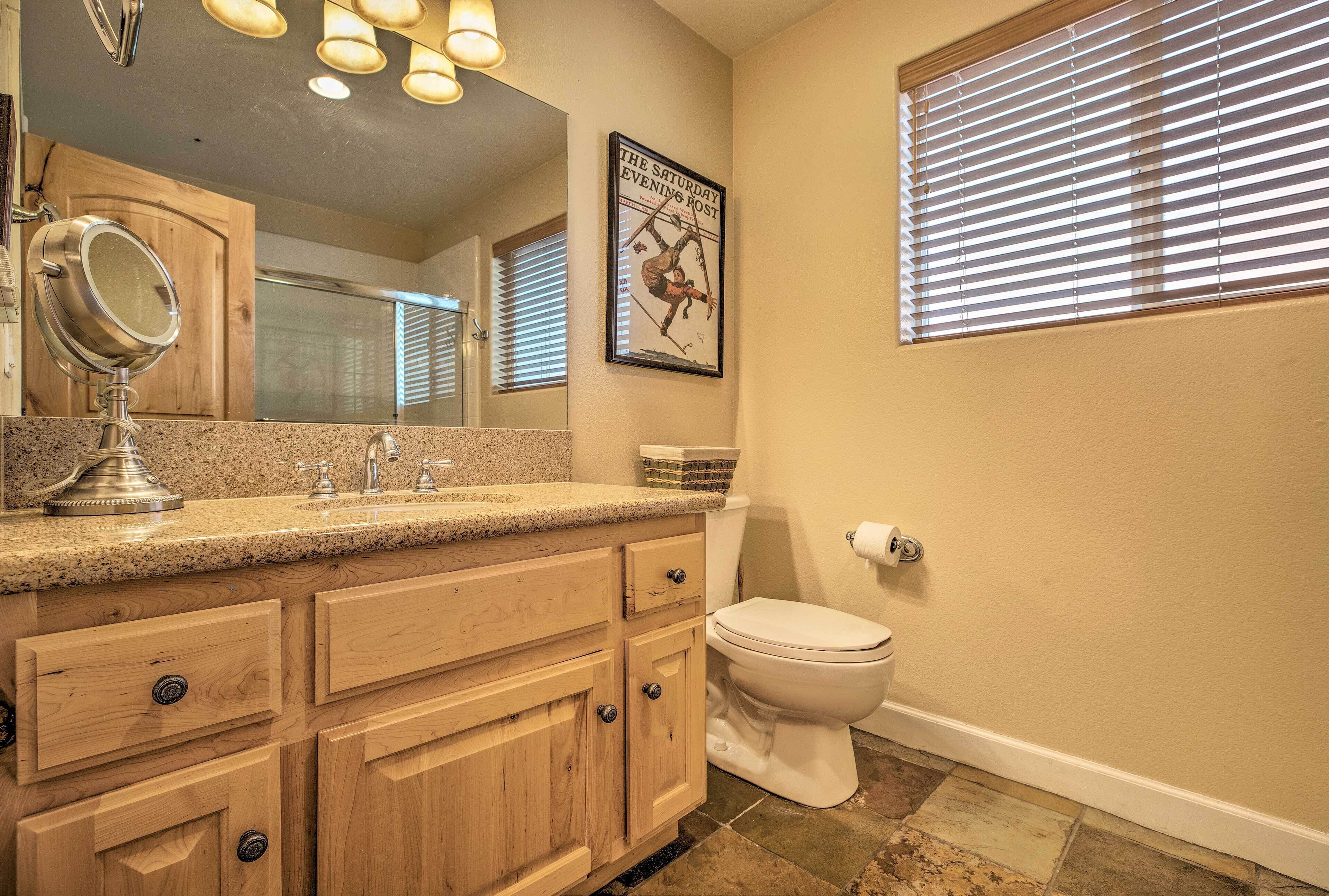 A bathroom with a granite countertop, wooden cabinets, a toilet, and a framed poster on the wall.