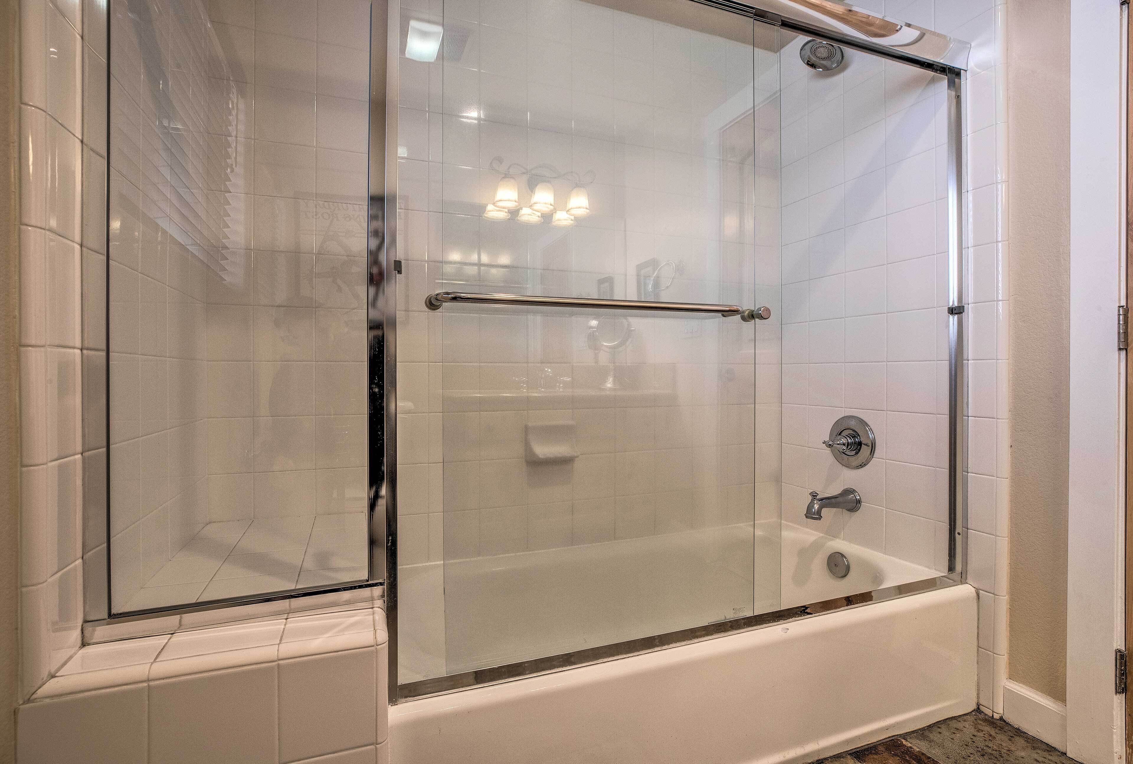 Eine begehbare Glasdusche mit Badewanne, weißen Fliesenwänden und einer Glastür.