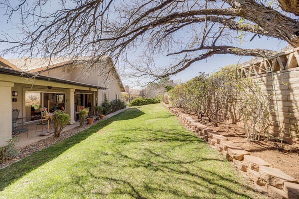 A house with a covered patio, a well-maintained lawn, and a stone wall. - Stunning Sedona Views: Spa, Firepit & Stargazing (Sedona)