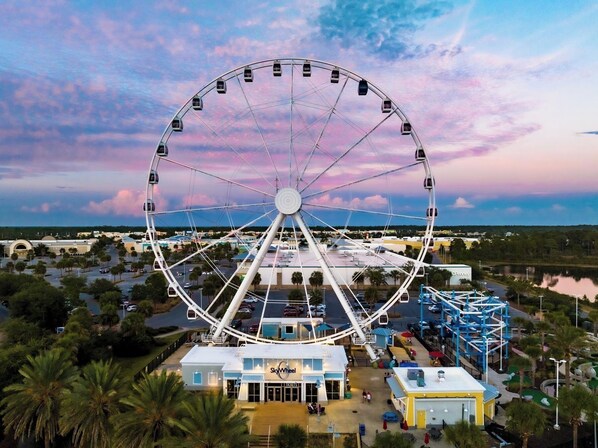Una noria grande con una taquilla de venta de boletos y un edificio que dice "SkyWheel" en primer plano.
