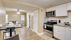 A modern kitchen with white cabinets, a black stove, and a microwave. There is a dining area with a table set for two and a coat rack. - 1 Mi to Dtwn Wilmington: Convenient + Cozy Home! (Wilmington)