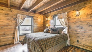 A wooden cabin bedroom with a bed, two windows with curtains, a wall-mounted lamp, and a wooden ceiling. - Hike, Hunt & Unwind: Mtn-view Cabin in Del Norte! (Del Norte)