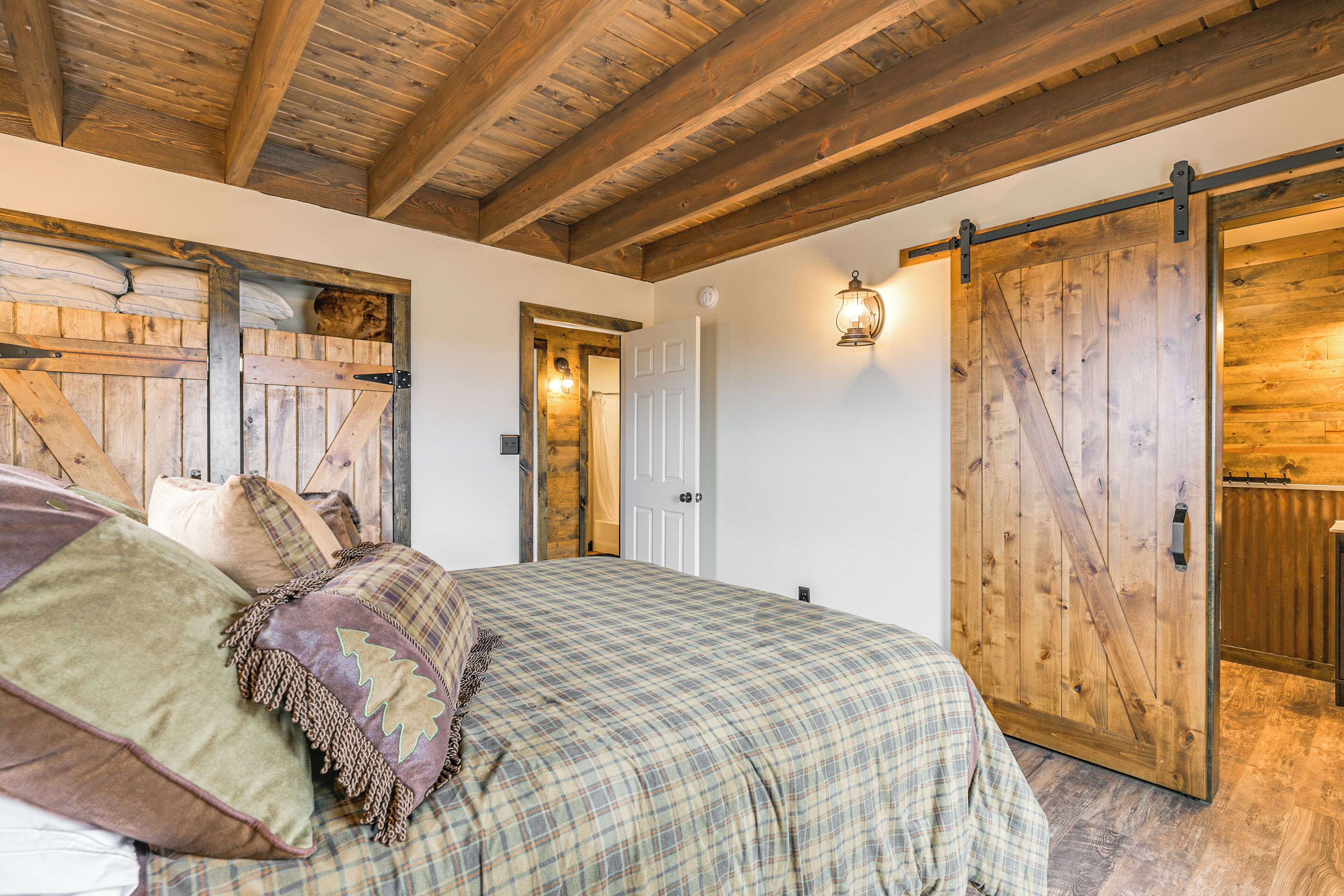 Une chambre à coucher dotée d’un grand lit, de poutres apparentes en bois au plafond, d’une porte coulissante de style grange et d’une décoration rustique.