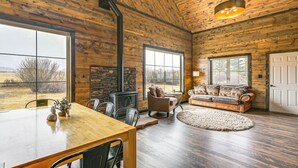 A spacious room with a wooden ceiling, large windows, a fireplace, a sofa, and a dining table. - Hike, Hunt & Unwind: Mtn-view Cabin in Del Norte! (Del Norte)