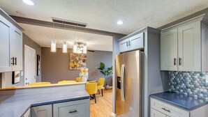 A modern kitchen with grey cabinets, a stainless steel refrigerator, and pendant lighting.