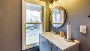 A bathroom with a window, sink, mirror, and light fixture.