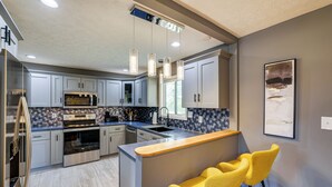 A modern kitchen with a central island, stainless steel appliances, and a bar area with yellow chairs.