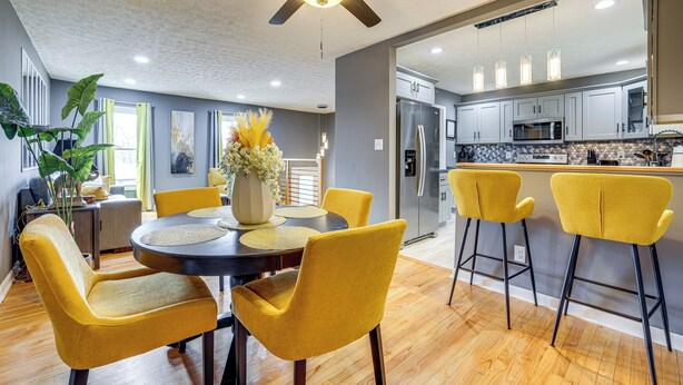 A modern kitchen with stainless steel appliances, a dining area with yellow chairs, and a ceiling fan.